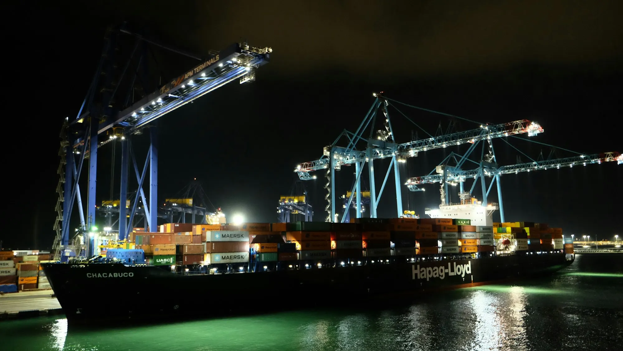 A container ship at a terminal at night under lit cranes